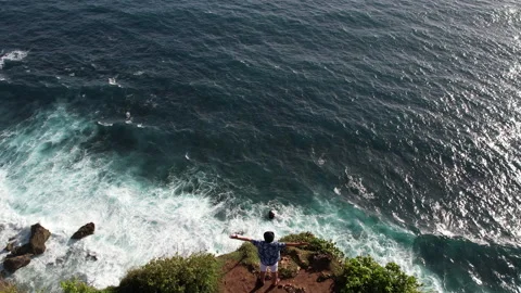 Man stand on edge of cliff, spread arms wide and looking into the endless ocean Stock Footage 269895384