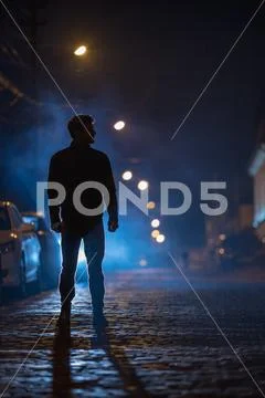 The man stand on the foggy street. Evening night time. Telephoto lens shot Stock Photos