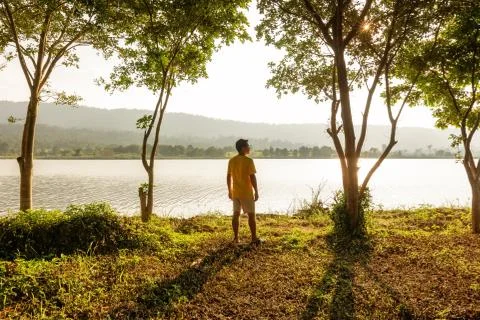 A man stand in the forest and near the water with mountain back. Stock Photos