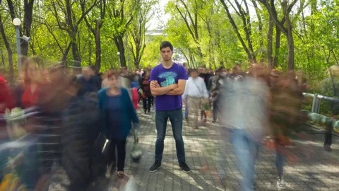The man stand in the ghost-like crowd flow, on background green trees . Time Stock Footage 80084784