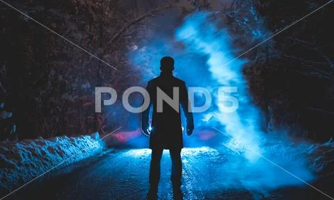 The man stand near the blue smoke on the snowy road. evening night time Stock Photos