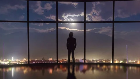 The man stand near a panoramic window on a background of a mountain. Time lapse Video stock 73446326