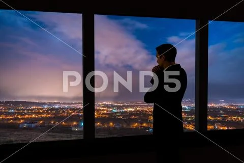 The man stand near the panoramic window. Evening night time Stock Photos