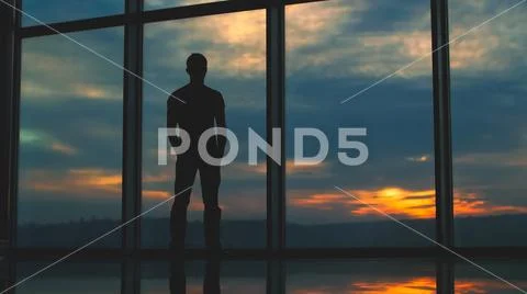 The man stand near the window on the background of sunset Stock Photos