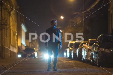 The man stand outdoor on the background of a headlight. Evening night time Stock Photos