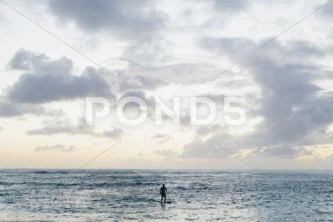 Man stand up paddling in calm waters at dusk Stock Photos