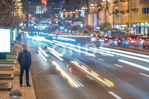 The man stand on the roadside against the background of traffic stream. Eve.. Stock Photos