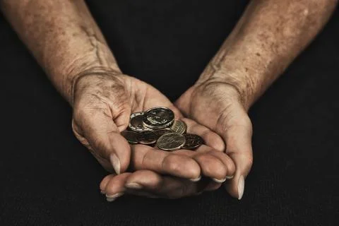 Man standing against a solid black background, holding money coins as a symbol o 写真素材