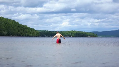 Man standing alone in lake stretching arms facing water Stock Footage 84804073