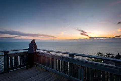 Man standing alone on view point by lake looking at sunset Stock Photos