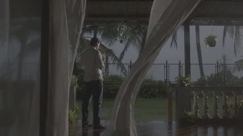 Man standing alone while it's raining outside with the curtains flying. Stock-Footage 90611351