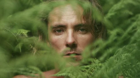Man standing and looking through the leaves straight at the camera Stock Footage 279852524
