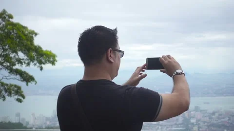 Man Standing Back on a Mountain Shoots by Phone Panorama of a City. Slow Motion Stock Footage 66381542