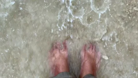 Man Standing Barefoot on Sandy Beach with Waves Washing Over Feet Stock-Footage 332749483