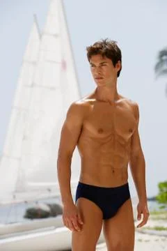Man standing in bathing suit in front sail boat Stock Photos