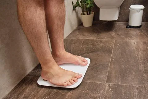 Man standing on bathroom scale measuring body weight on tiled floor. Weight l Stock Photos
