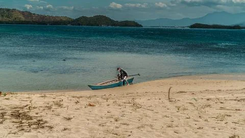A man is standing on the beach next to a small boat Stock Photos