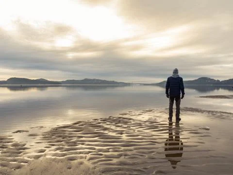 Man standing at the beach, reflections of the man in the water. Calm sea, mist Stock Photos