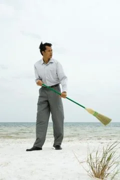 Man standing on beach sweeping with broom, looking away Stock Photos