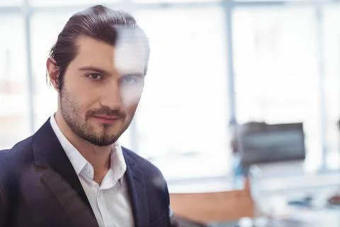Man standing behind glass partition at modern office desk, viewing computer Stockfoto's
