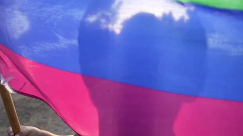 Man standing behind rainbow flag waving in the wind backlighted silhouette 스톡 동영상 250474065