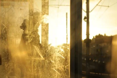 A man standing behing dirty and scratched glass at a trainstation in backligh 스톡 사진