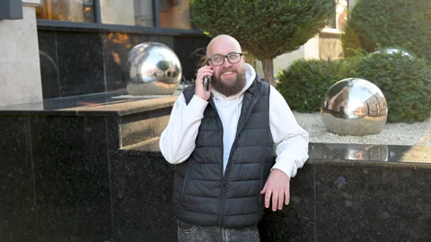 Man standing beside shiny spheres while talking on phone outside modern building Stock Footage 346768348