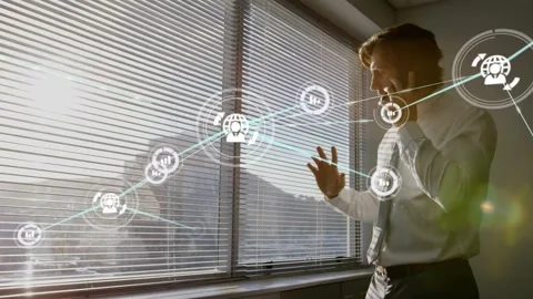 Man standing at blinds window holding phone and gesturing, causing node network Stock Footage 334036810
