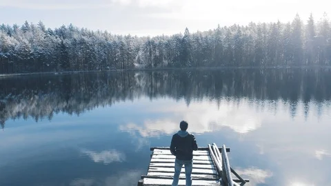 Man standing on the bridge in beautiful winter lake surrounded by forest Stock Footage 105420774