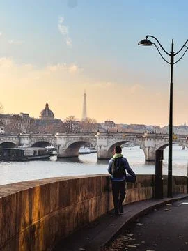 A man standing on a bridge overlooking a river with a Paris in the background. Stock Photos