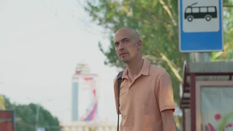A man standing at a bus stop in the middle of the city puts a medical mask on Stock Footage 154735930