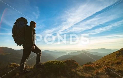 The man standing with a camping backpack on the rock with a picturesque sunse Stock Photos