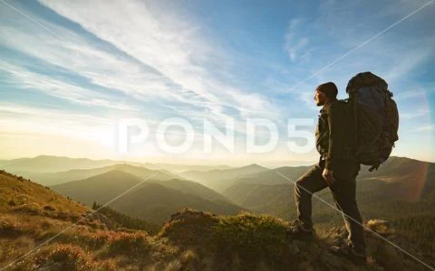 The man standing with a camping backpack on the rock with a picturesque sunri Stock Photos