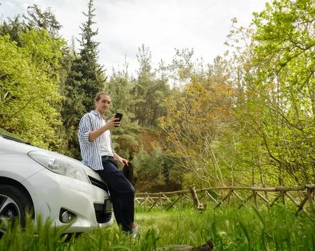 Man standing by car and using smartphone. Stock Photos