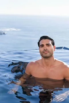Man standing chest-deep in infinity pool, shirtless, facing lens with ocean Stock Photos