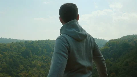 Man standing on cliff edge and looking out over lush green forest, Stock Footage 280127166