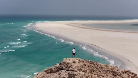 Man standing on a cliff edge enjoying pristine beach view, socotra island Vidéo 334674281