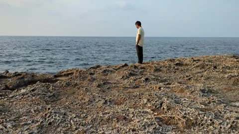 Man standing by the cliff looking at the water. Tilt up shot. Stock Footage 267688144