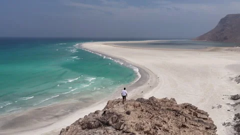Man standing on a cliff overlooking a tropical beach Stock Footage 334677517