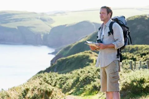 Man standing on cliffside path holding map Stock Photos