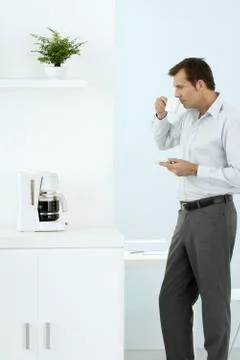 Man standing by coffee maker, taking a sip of coffee, holding saucer Foto stock