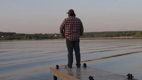 Man standing on a dock on the river on a summer evening at sunset, rear view Stock Footage 276722759