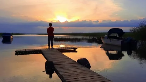 A man standing on a dock watching the sun set,  lake, beautiful boy Stock Footage 280892240