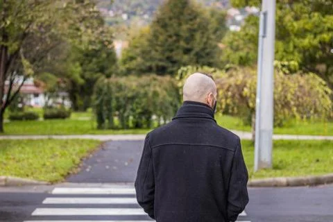 A man is standing in the dripping rain while wearing a mask at pedestrian cro Stock Photos