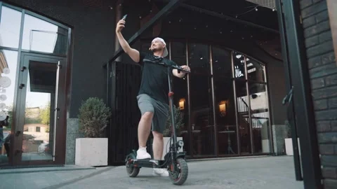 Man standing with e-scooter in city downtown and taking selfie with smartphone Stock Footage 229257438