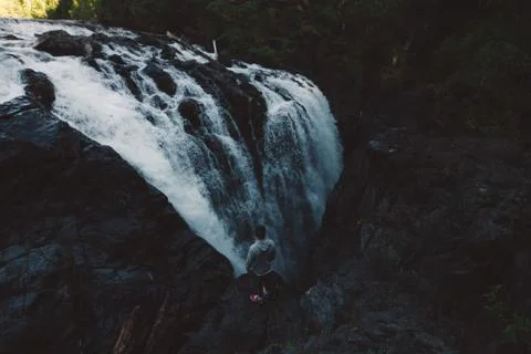 Man standing on the edge of the cliff in forest with waterfall Stock Photos