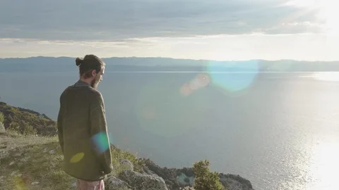 Man standing on the edge of a cliff looking to the ocean in dawn and walking Stock Footage 121806295
