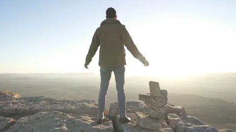 Man standing on the edge of a desert cliff lifts his hands up Stock Footage 73081819