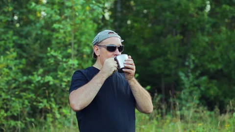 A man is standing on the edge of the forest drinking tea from a mug and admiring Stock Footage 94153150