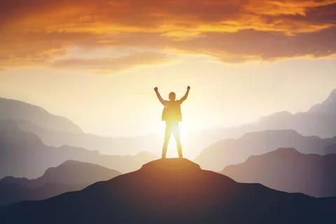 Man standing on edge of mountain feeling victorious with arms up in the air. Stock Photos